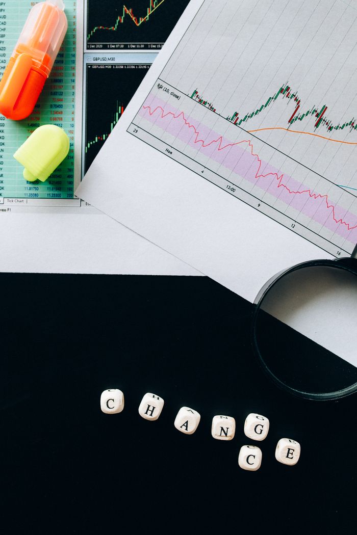 A flat lay image featuring financial charts, highlighters, and dice spelling 'CHANGE' on a black background.