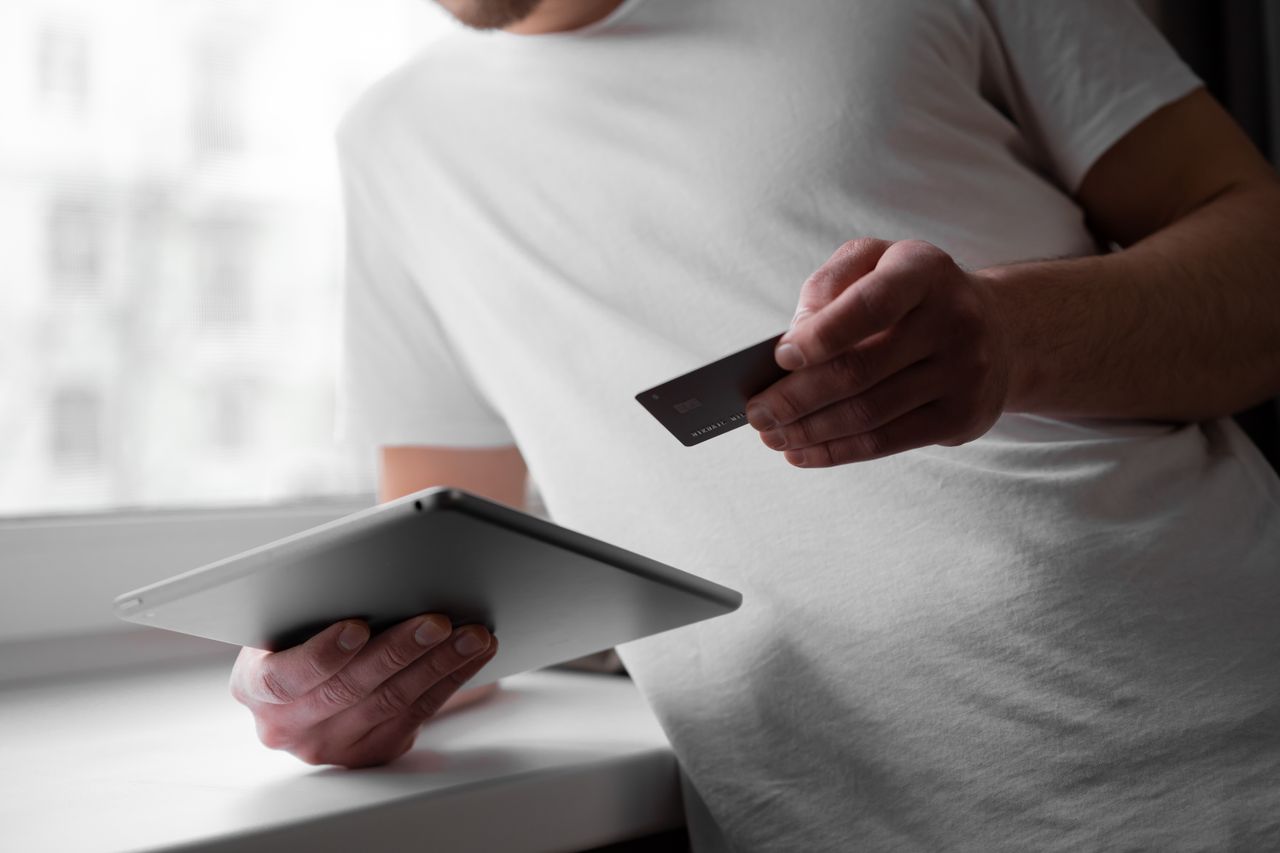 Man in a white shirt using a tablet and credit card indoors for online transaction.